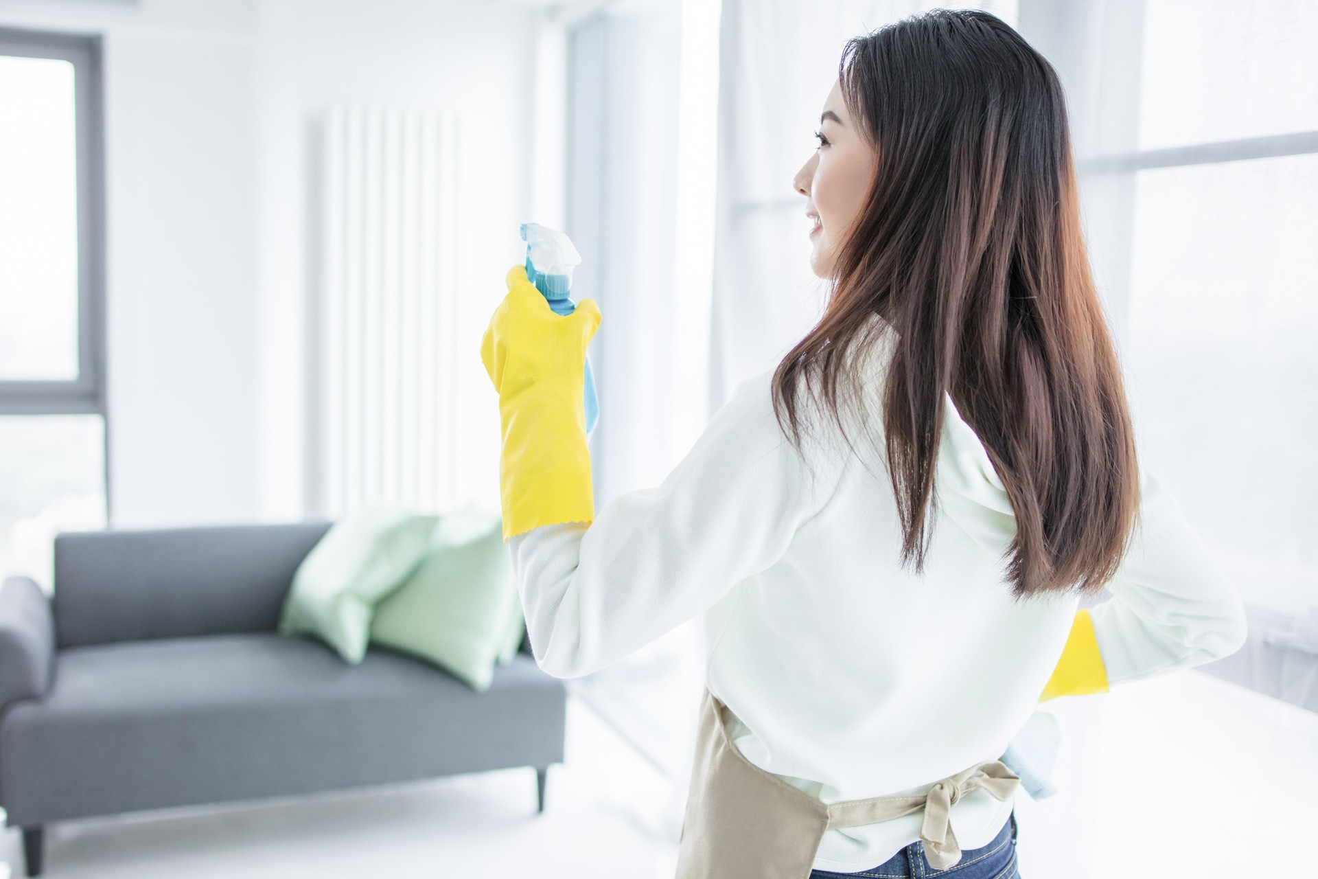 Asian woman cleaning house with spray bottle and rubber gloves